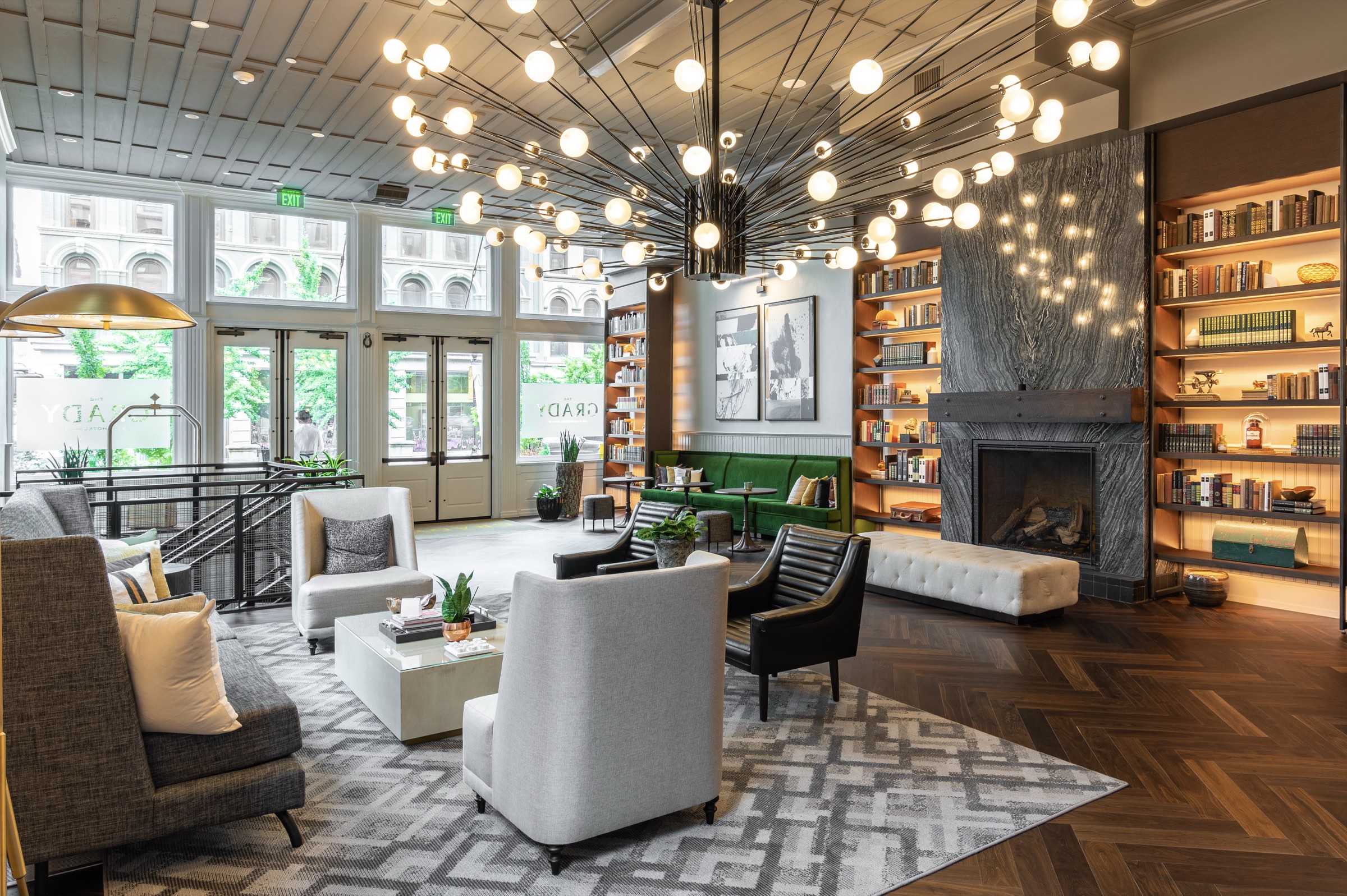 Hotel lobby with a starburst globe chandelier, marble fireplace, lit bookshelves and custom lounge seating