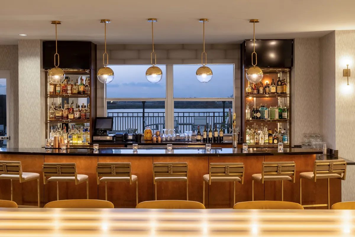 Hotel bar with brass pendant lights, backlit shelving and waterfront views