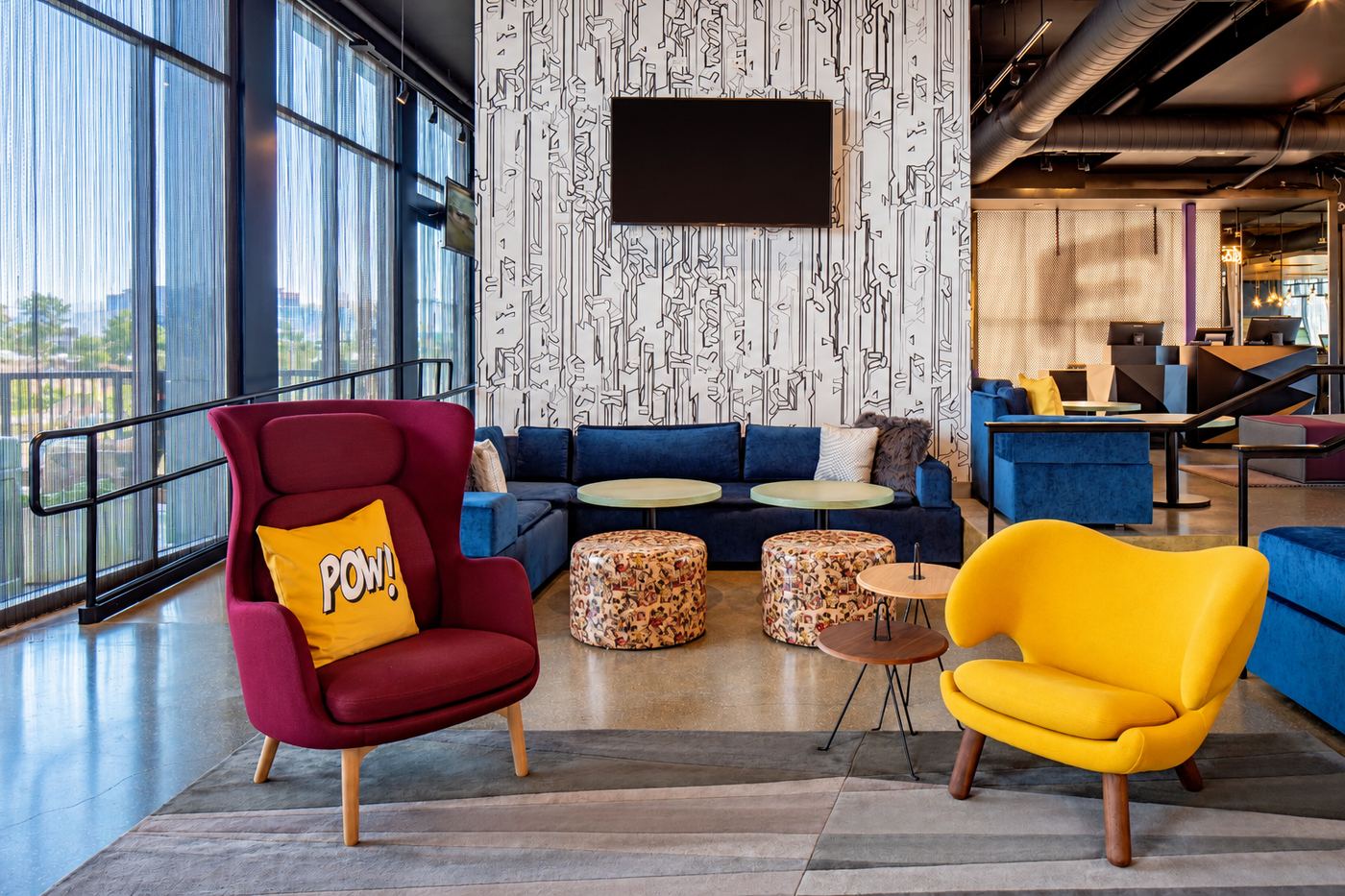 Hotel lounge with blue banquette seating, colourful accent chairs and patterned feature wall